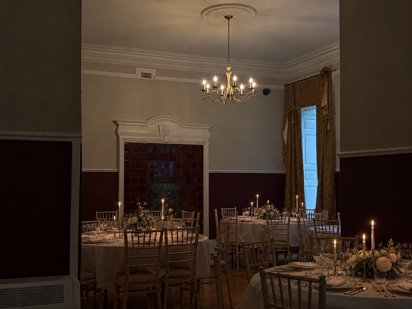 The Dining Hall by candlelight, with tables laid for dinner and a tiled fireplace