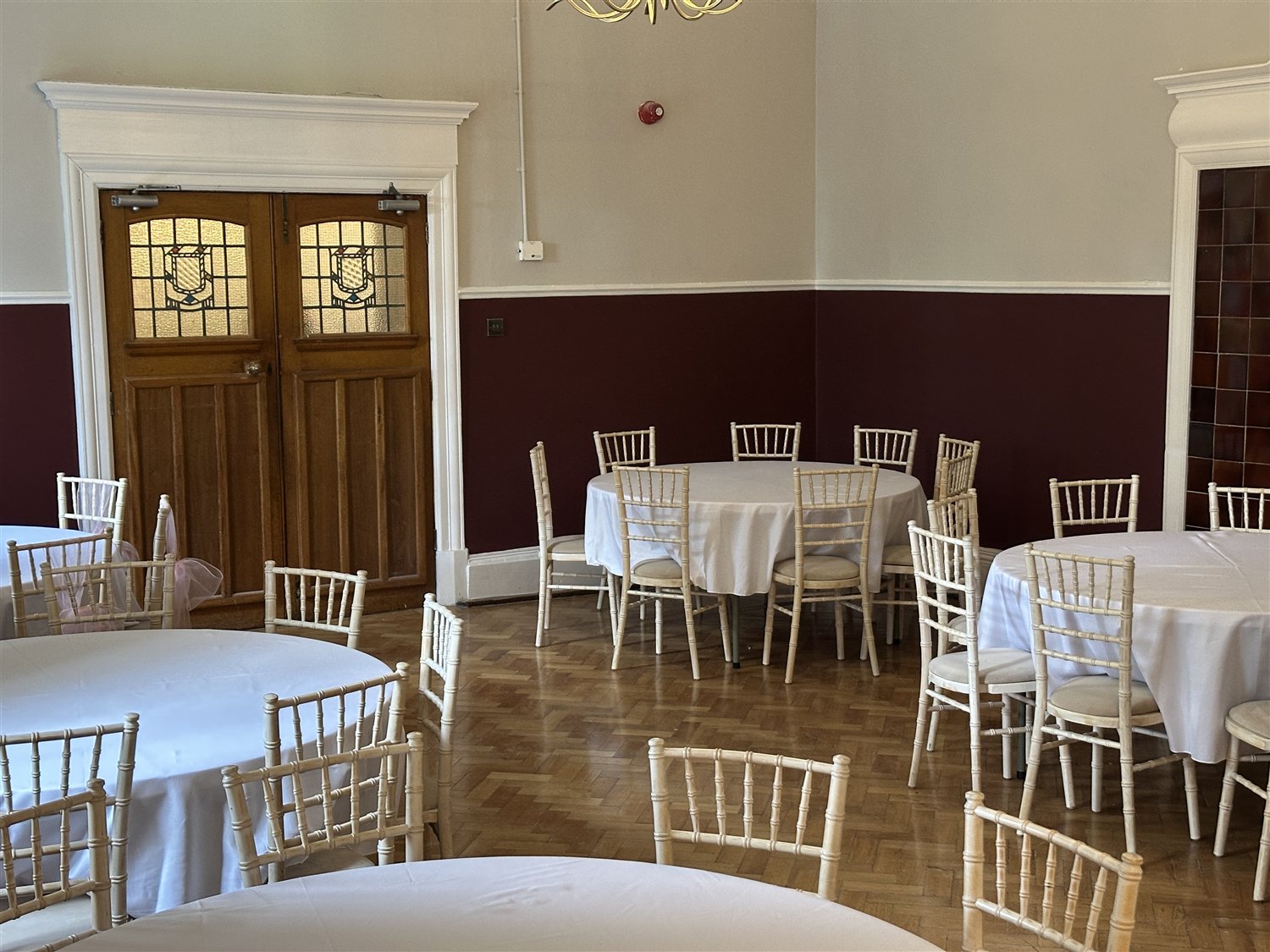 Round tables and limewash chairs beside the Dining Hall's stained glass double doors