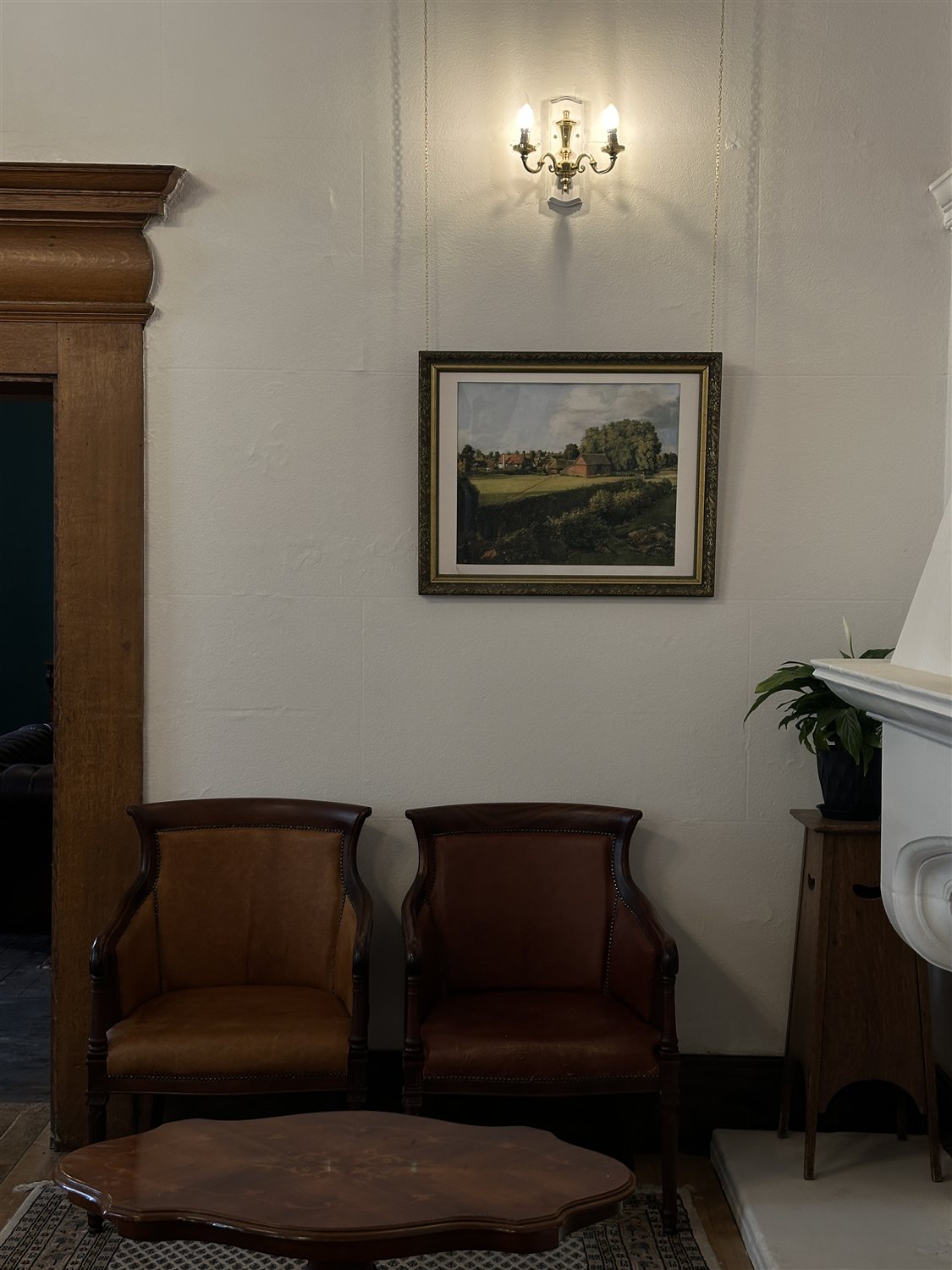 Two leather chairs beneath a framed landscape painting and brass wall light