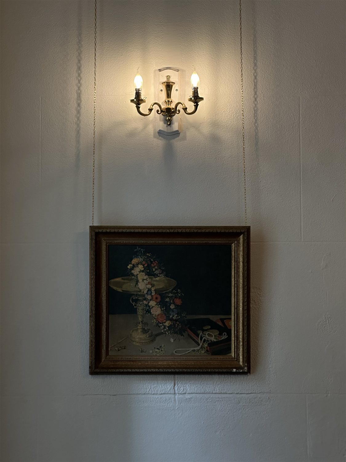 A brass wall light above a framed still-life painting