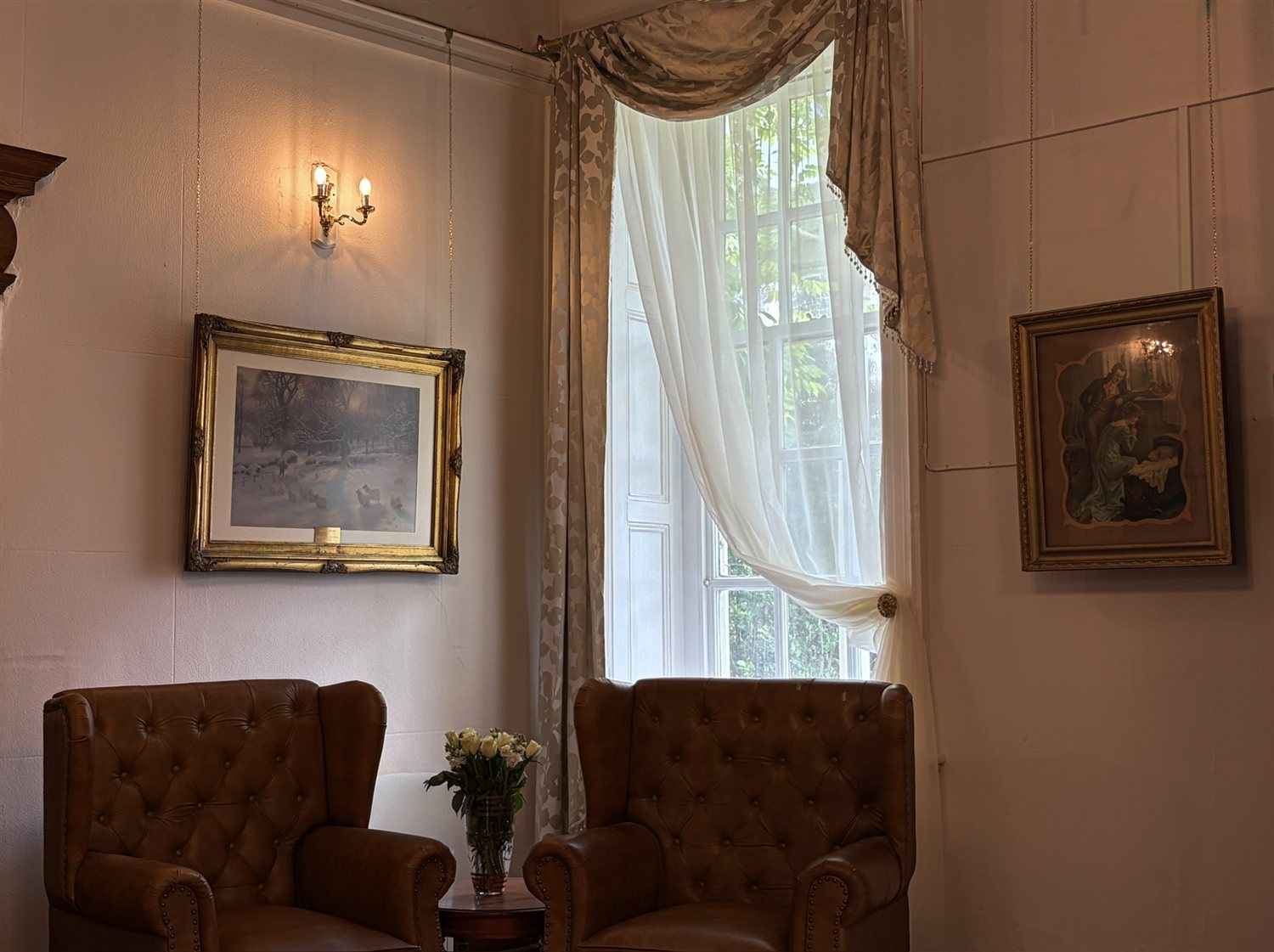 Leather wing chairs beside a tall draped window, with framed paintings and wall lights