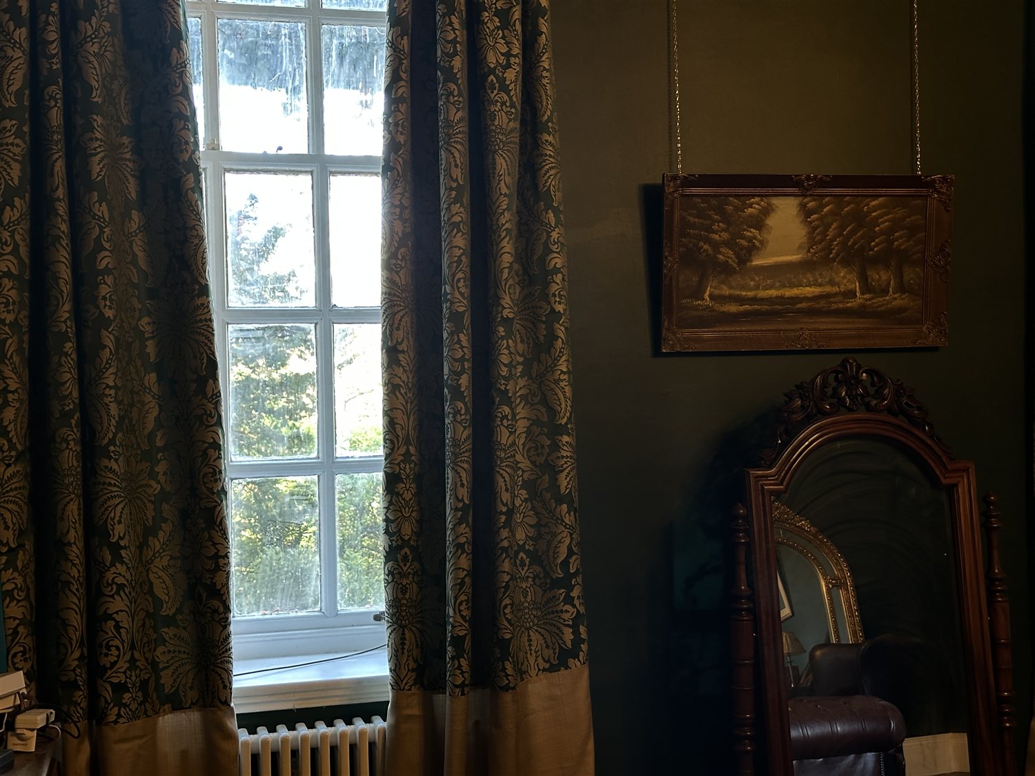 Damask curtains at a sash window beside a framed landscape and antique mirror