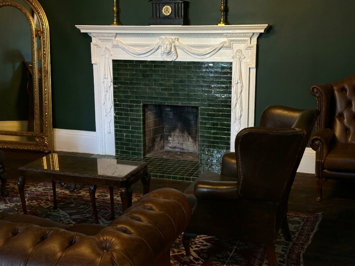 The Green Room's white fireplace with green tiles, leather sofas and a gilt mirror