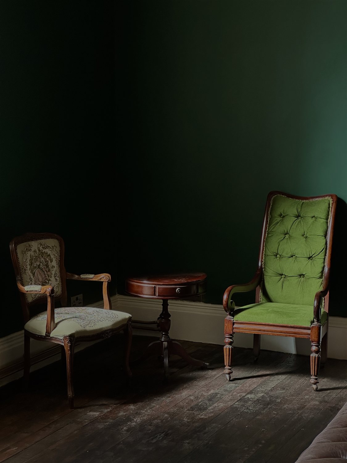 Two antique armchairs and a drum table against the Green Room's deep green walls